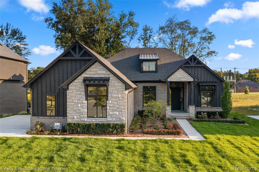 Modern farmhouse style home featuring board and batten siding, stone siding, and a front lawn