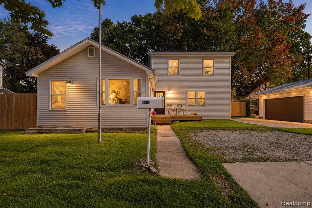 White siding exterior, front lawn, concrete walkway, gravel driveway, and a detached garage with a dark door