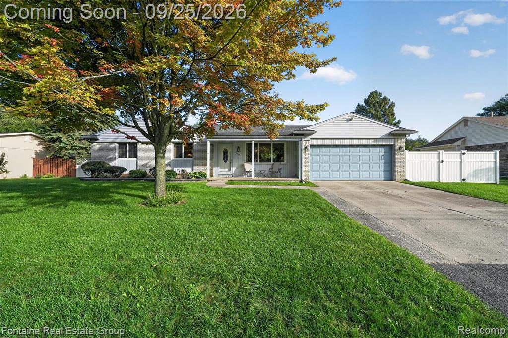 Ranch-style residence featuring a prominent front lawn, concrete driveway, and attached garage with a panel door
