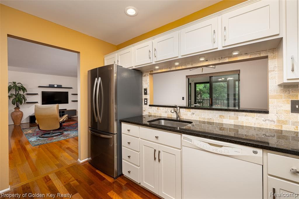 Kitchen featuring white cabinetry, dark countertops, a stainless steel refrigerator, and a tiled backsplash