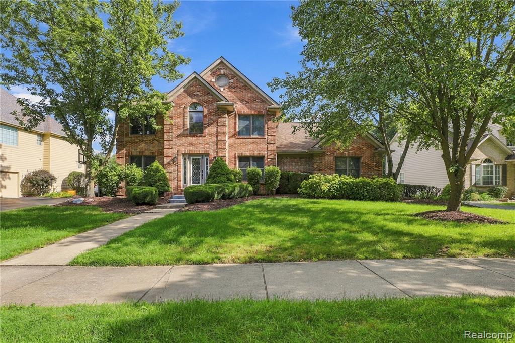 Brick facade, arched window over entryway, established front yard landscaping, mature trees, concrete walkway