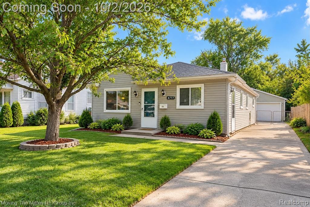 Single-story residence with siding exterior, mature front yard tree, concrete driveway, and detached garage