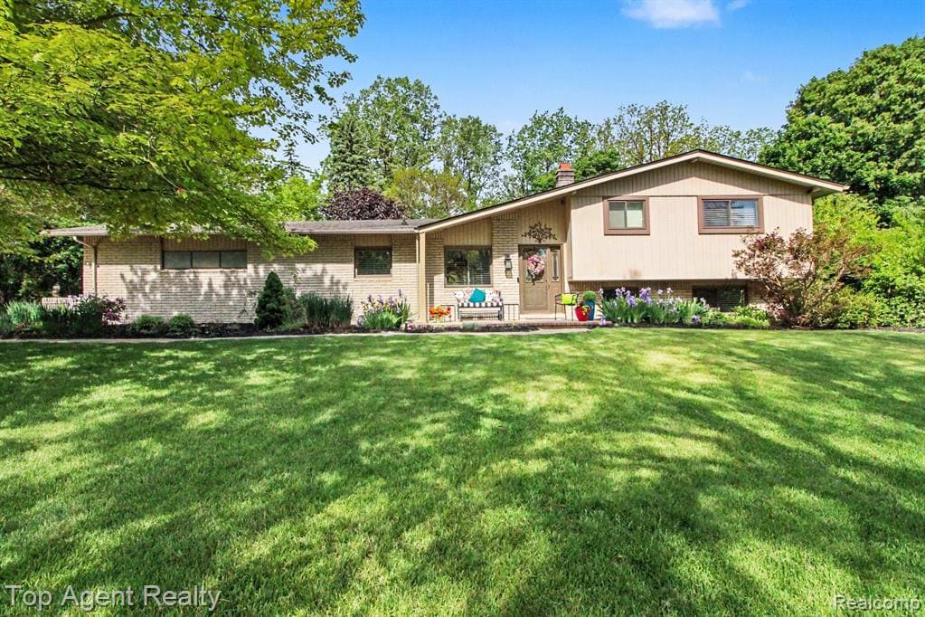 Split-level residence featuring brick and siding exterior, front entry with covered porch, and extensive front lawn