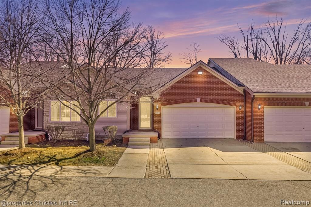 Ranch-style house featuring a shingled roof, driveway, an attached garage, and brick siding