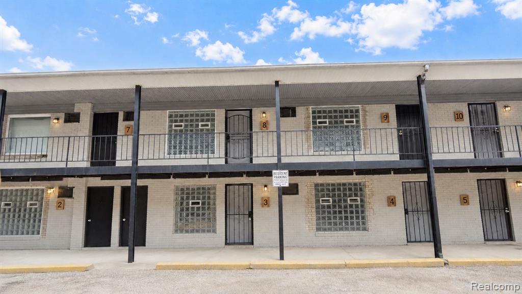 Two-story building with white brick facade, black metal railings, glass block windows, and black security doors