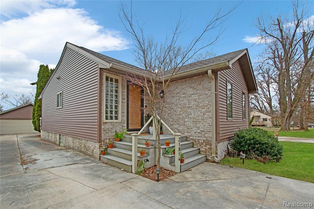 Exterior featuring horizontal siding, a gabled roofline, a concrete driveway, and established plantings