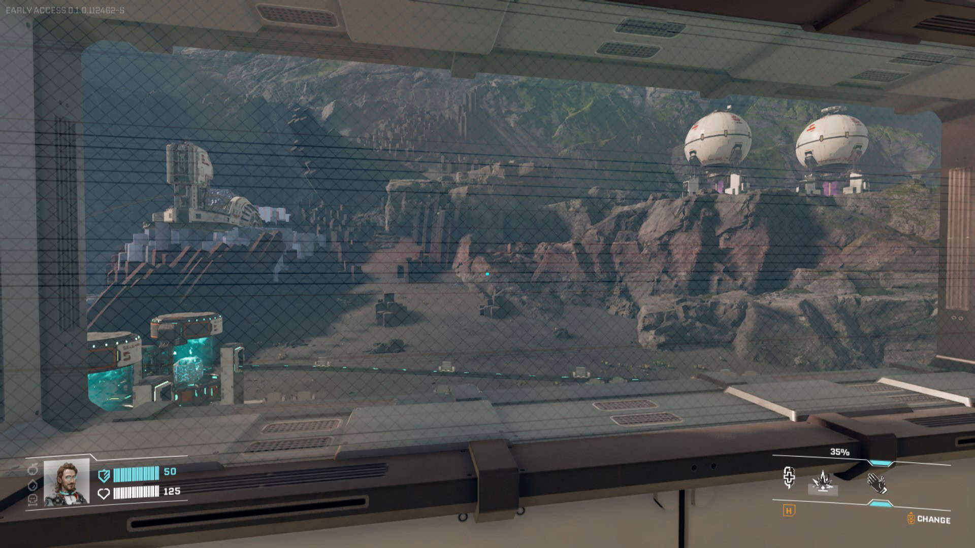 A number of industrial structures and mining equipment along a rocky ridge, as seen from inside a building through a window.