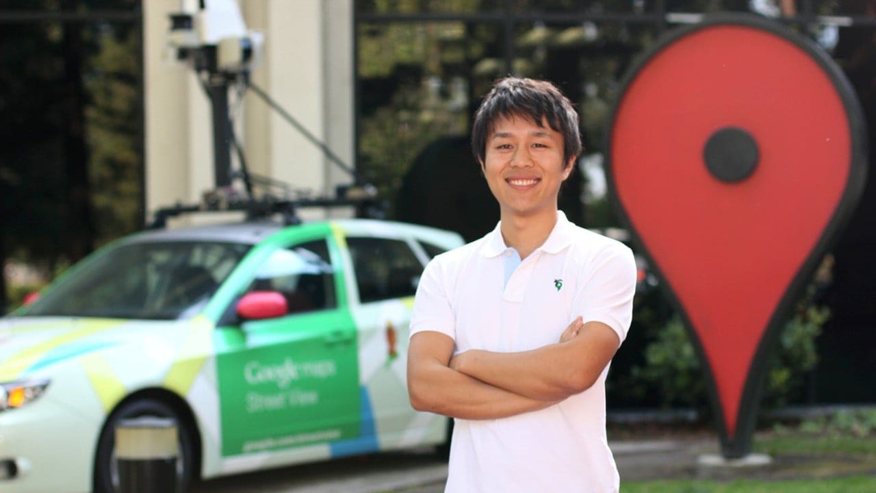 Tatsuo Nomura standing in front of a Google Maps car and a statue of an icon from Google Maps