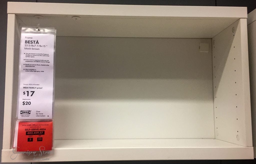 An empty IKEA shelving unit frame in black-brown, priced at $17 for IKEA Family members or $20 regularly. Perfect for an IKEA Desk Hack, this versatile shelf is on display in-store, awaiting your creativity to transform it into a functional workspace masterpiece.