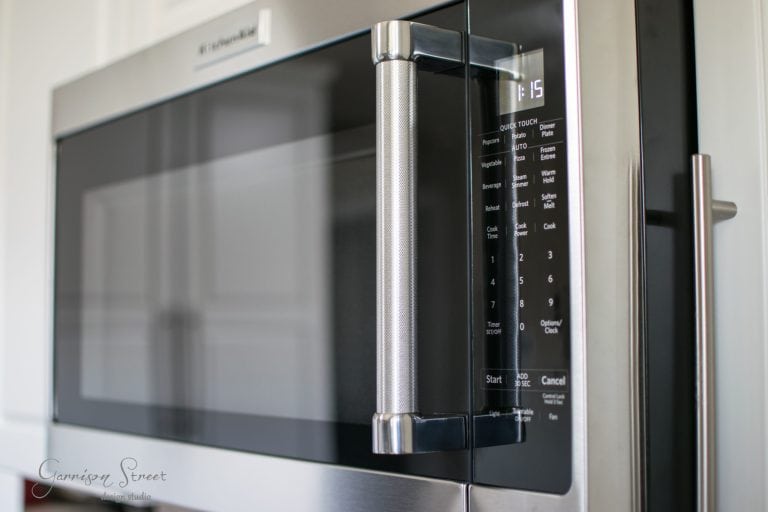 Close-up of a stainless steel microwave with a digital keypad and display screen on the right. The microwave's handle is prominently featured, reflecting the kitchen environment around it.