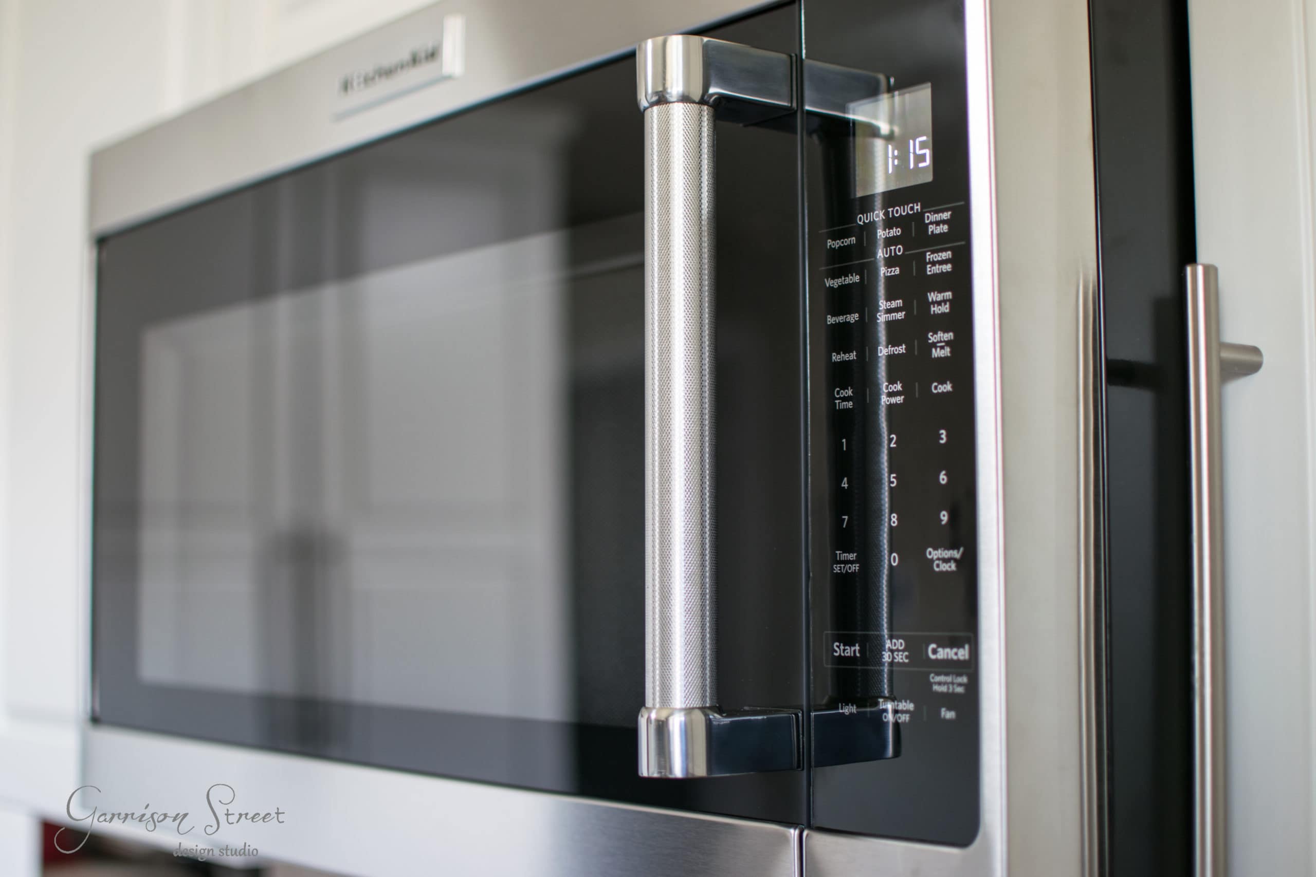 Close-up of a stainless steel microwave with a digital keypad and display screen on the right. The microwave's handle is prominently featured, reflecting the kitchen environment around it.