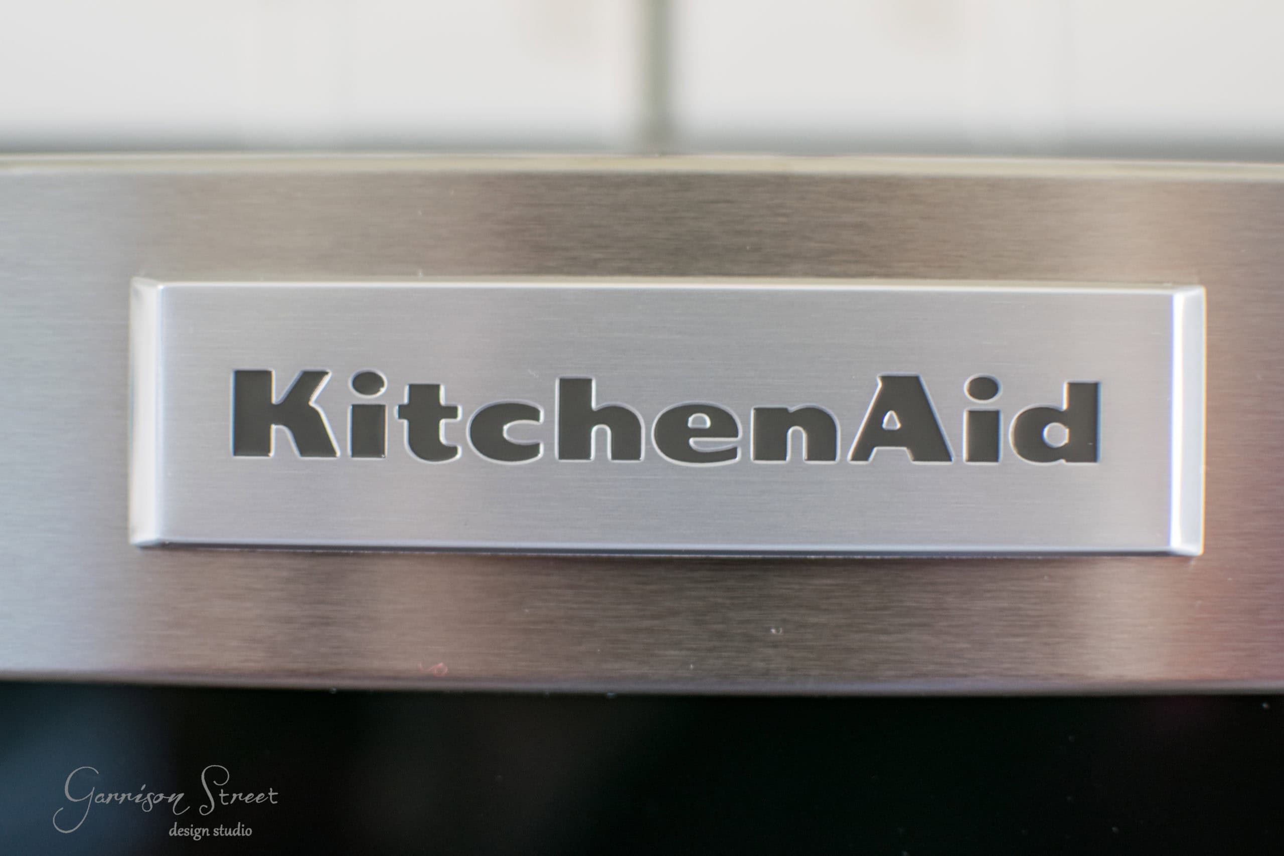 Close-up of a stainless steel KitchenAid logo on an appliance. The brand name is prominently displayed on a shiny surface with a brushed metal texture.