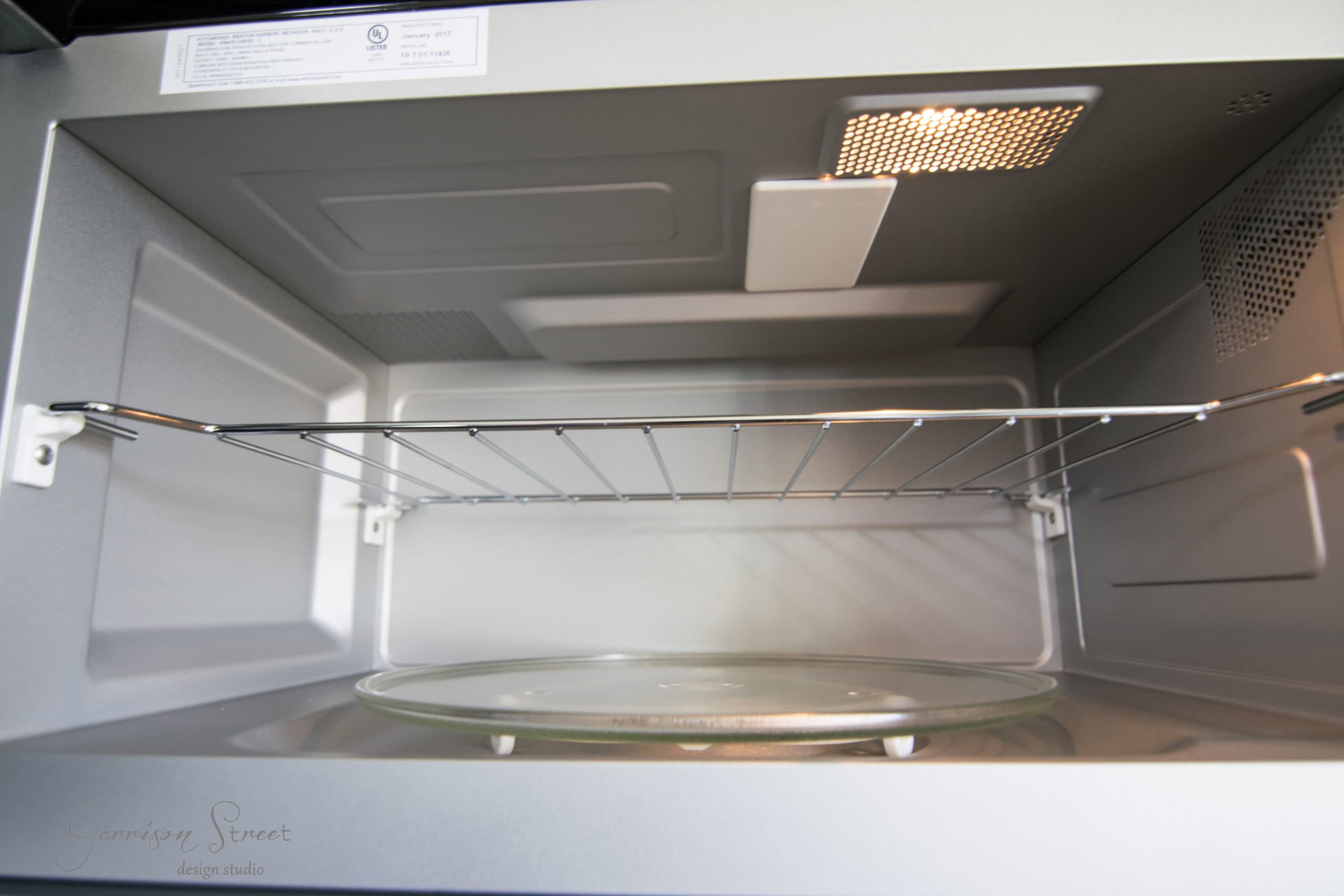 A clean, empty microwave oven with an interior light on, showing its turntable and metal rack inside. The microwave door is open, revealing details of its interior design and construction.