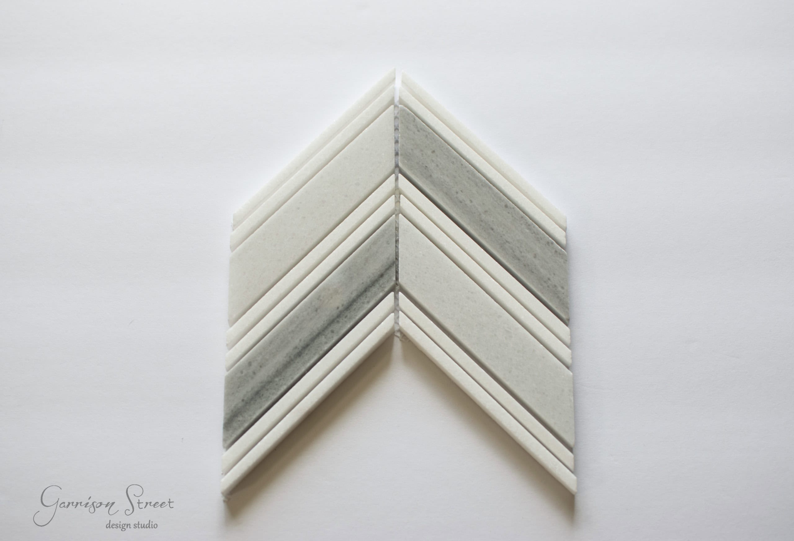 A V-shaped pattern made of alternating gray and white marble tiles on a plain white background. The geometric design has a smooth, polished finish, showcasing a modern and sleek style.