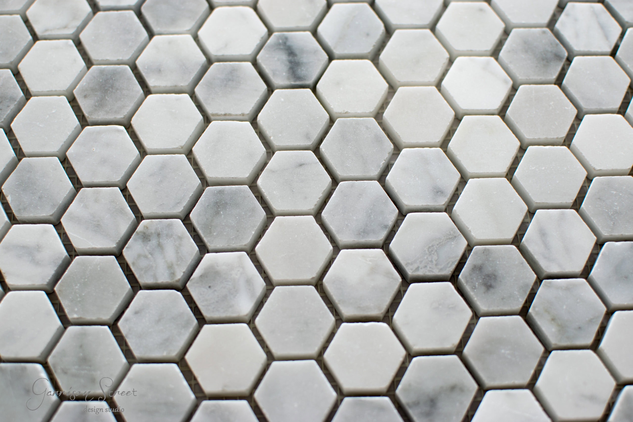 Close-up of a mosaic tile pattern featuring hexagonal tiles in shades of white, gray, and light beige, creating a textured surface.