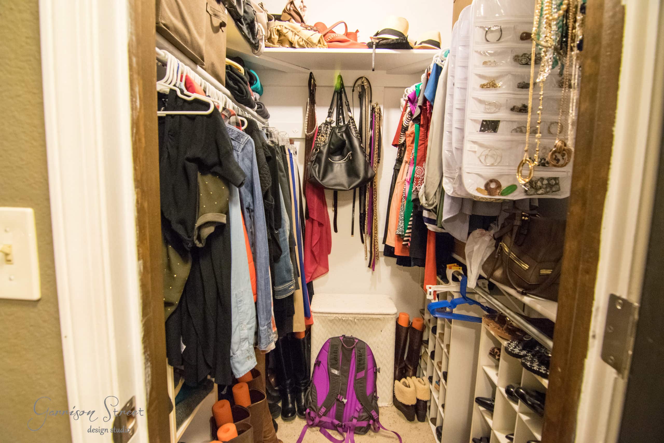A well-organized walk-in closet featuring hanging clothes, boots, and neatly arranged bags and accessories. Shelves on the sides hold shoes and purses, while a purple backpack rests on the floor.