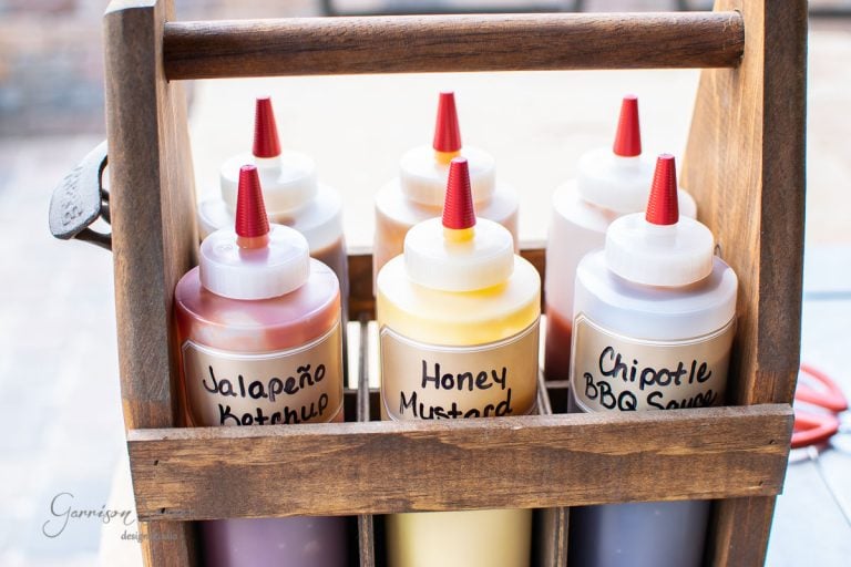 A condiment caddy showcases six squeeze bottles with red nozzles, each labeled Jalapeño Ketchup, Honey Mustard, and Chipotle BBQ Sauce. Bright and orderly display on a sunny day.