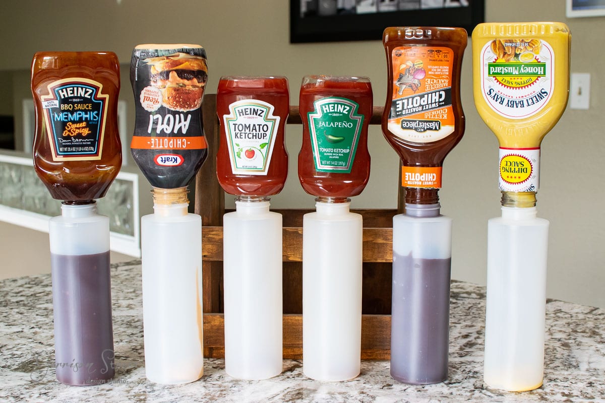 Six condiment bottles are neatly organized in a convenient condiment caddy on the kitchen counter. The bottles, showcasing visible brand labels, hold a variety of flavors like ketchup, BBQ sauce, and hot sauce.