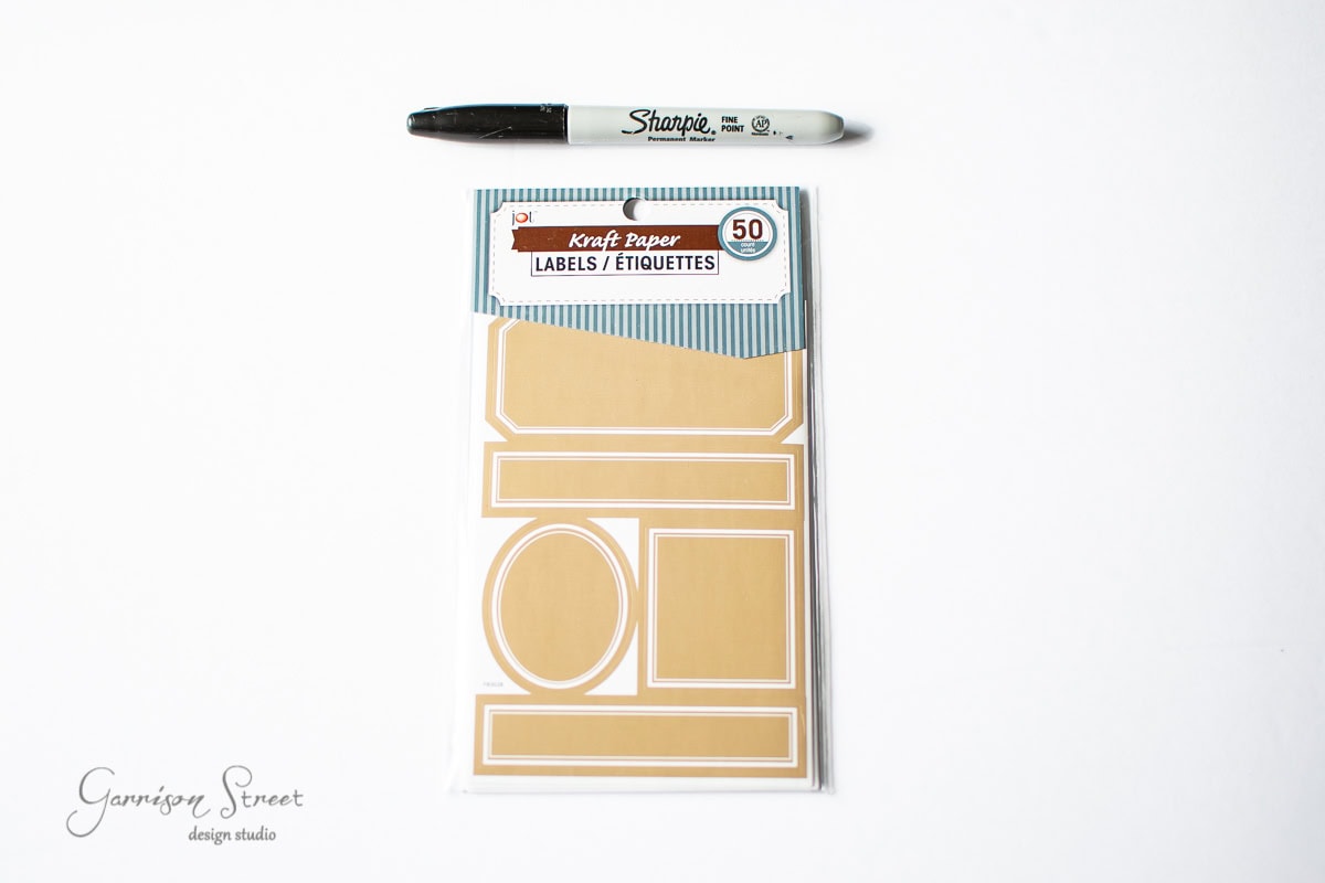 A black Sharpie marker and a pack of 50 kraft paper labels adorn a white background. With various shapes like rectangles and circles, these are perfect for organizing.