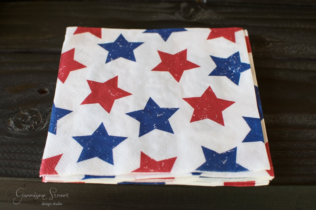 A stack of white napkins with red and blue stars printed on them, placed on a dark wooden surface.