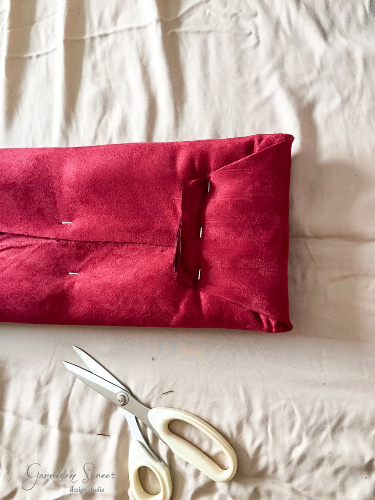A red cloth is folded neatly with pins holding the folds on a white fabric background. A pair of white-handled scissors is placed nearby.