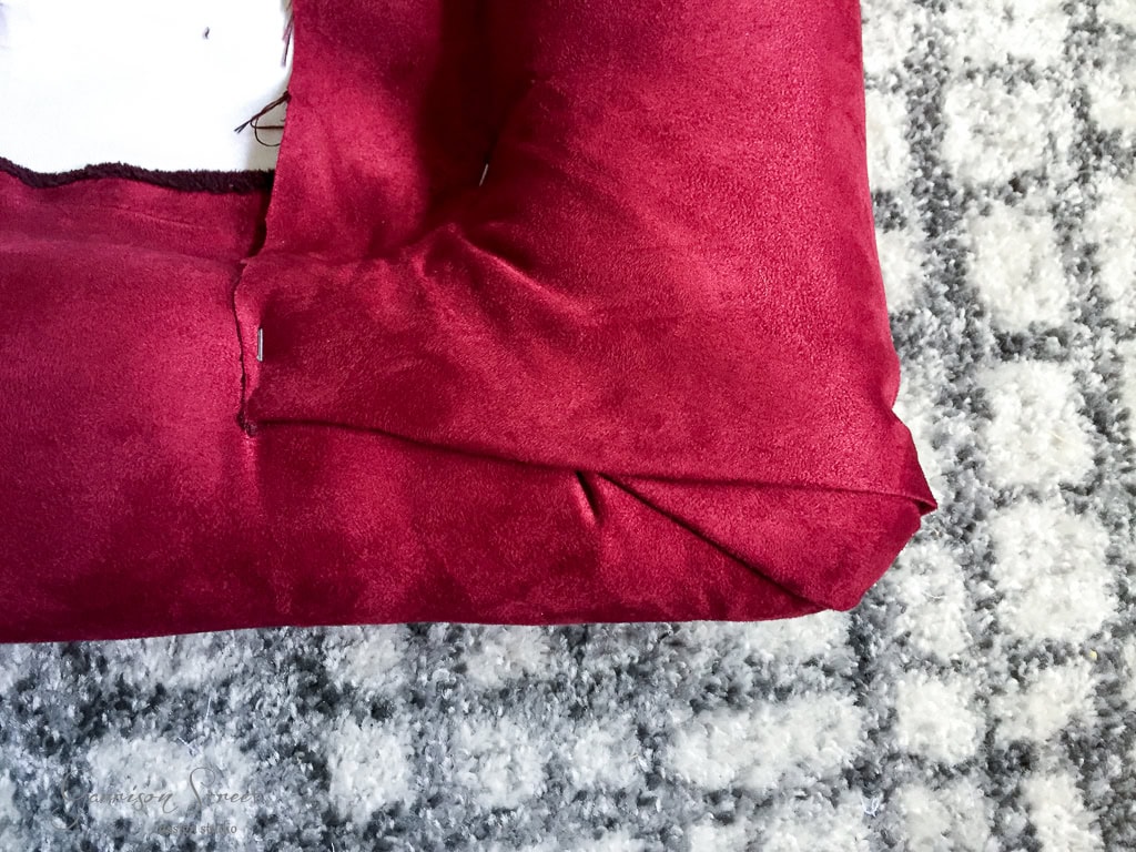 Close-up of a red upholstered couch corner with visible seams. The texture appears soft and velvety. The couch is set against a gray and white patterned carpet.