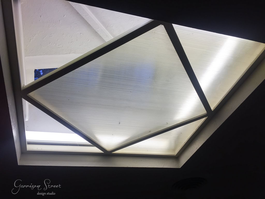 A view of a partially open skylight with a translucent cover, allowing some light to filter through. The geometric design of the skylight is surrounded by a triangular support structure.