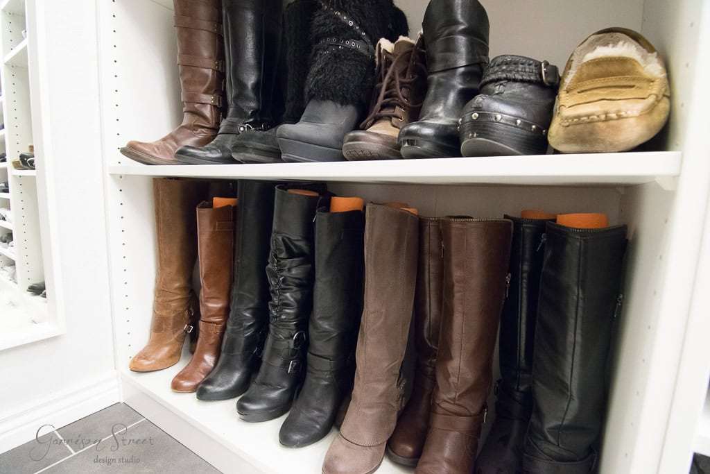 A neatly organized IKEA shoe rack showcasing various styles of boots and shoes enhances any walk-in closet. The top shelf features short boots and slippers, while the bottom shelf displays tall boots in different shades of brown and black.