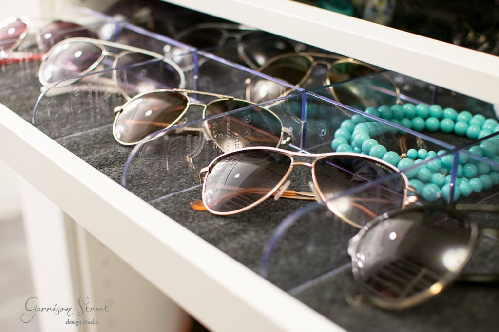 In a well-organized IKEA walk-in closet, a collection of aviator sunglasses with various lens tints rests neatly in a drawer. A turquoise beaded necklace adds a vibrant touch of color to the stylish scene.