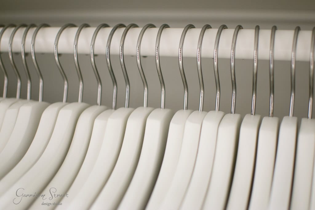 A row of identical white IKEA hangers is neatly aligned on a metal rod inside a walk-in closet, conveying a sense of order and organization.