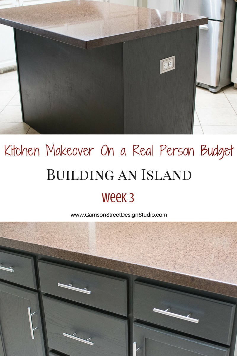 A modern kitchen island crafted from base cabinets, showcasing a brown countertop and sleek drawers with silver handles. A banner above reads, "How to Make a Kitchen Island on a Real Person Budget: Building an Island, week 3." Website link at the bottom.