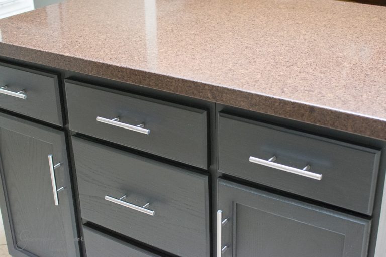 A dark wood kitchen cabinet with a brown polished countertop is shown, inspired by ideas on how to make a kitchen island out of base cabinets. The cabinet features multiple drawers and doors with sleek silver handles.