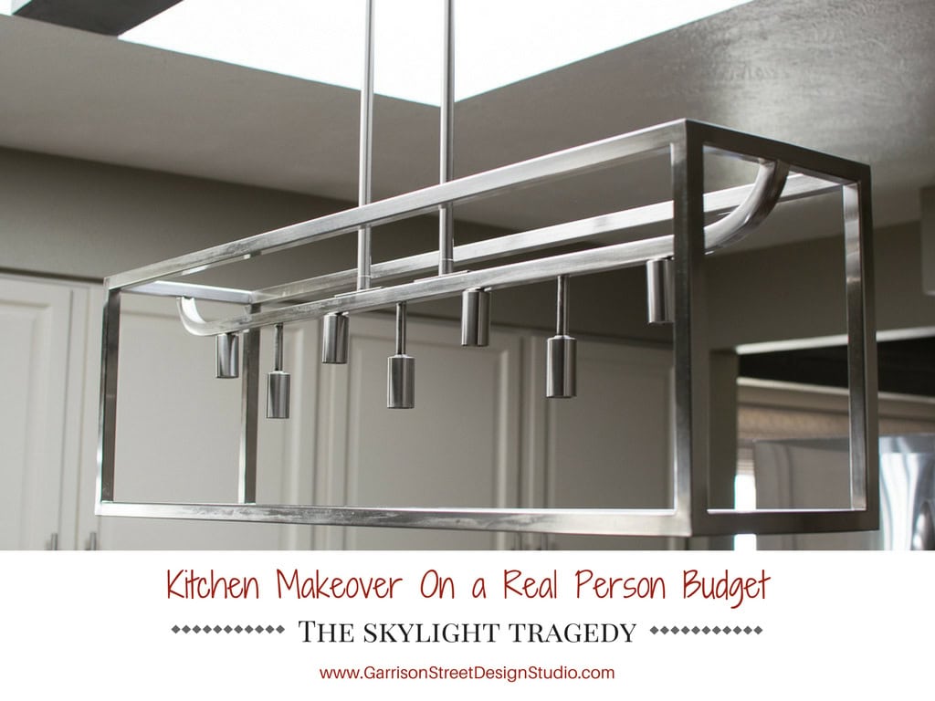A modern rectangular metal chandelier with multiple hanging lights is suspended above a kitchen, highlighting the skylight. The image features text: "Kitchen Makeover On a Real Person Budget - The Skylight Tragedy.