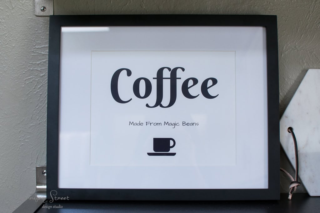 A framed sign with the word "Coffee" in large letters, accompanied by the phrase "Made From Magic Beans" in smaller text. Below, there's a simple black icon of a steaming coffee cup.