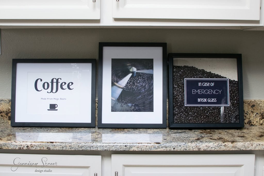Three framed coffee-themed pictures on a granite countertop. The first reads "Coffee" with a cup icon, the middle shows coffee beans close-up, and the third says "In case of emergency break glass" with beans behind glass.
