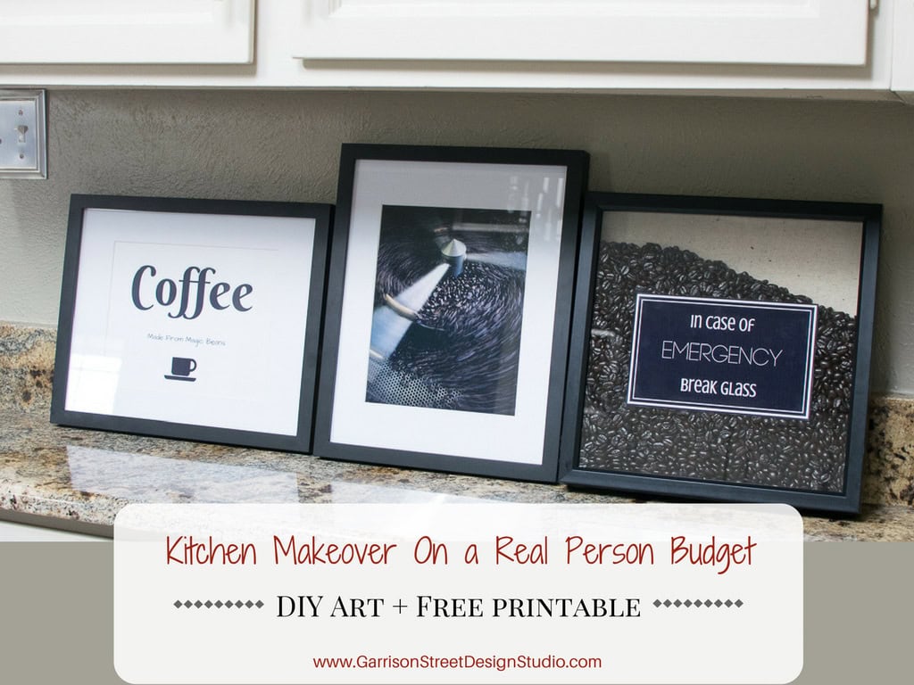 Three framed prints are displayed on a kitchen counter. One features the word "Coffee," another shows a coffee cup, and the third says "In case of emergency break glass" with coffee beans. A sign below reads "Kitchen Makeover On a Real Person Budget.