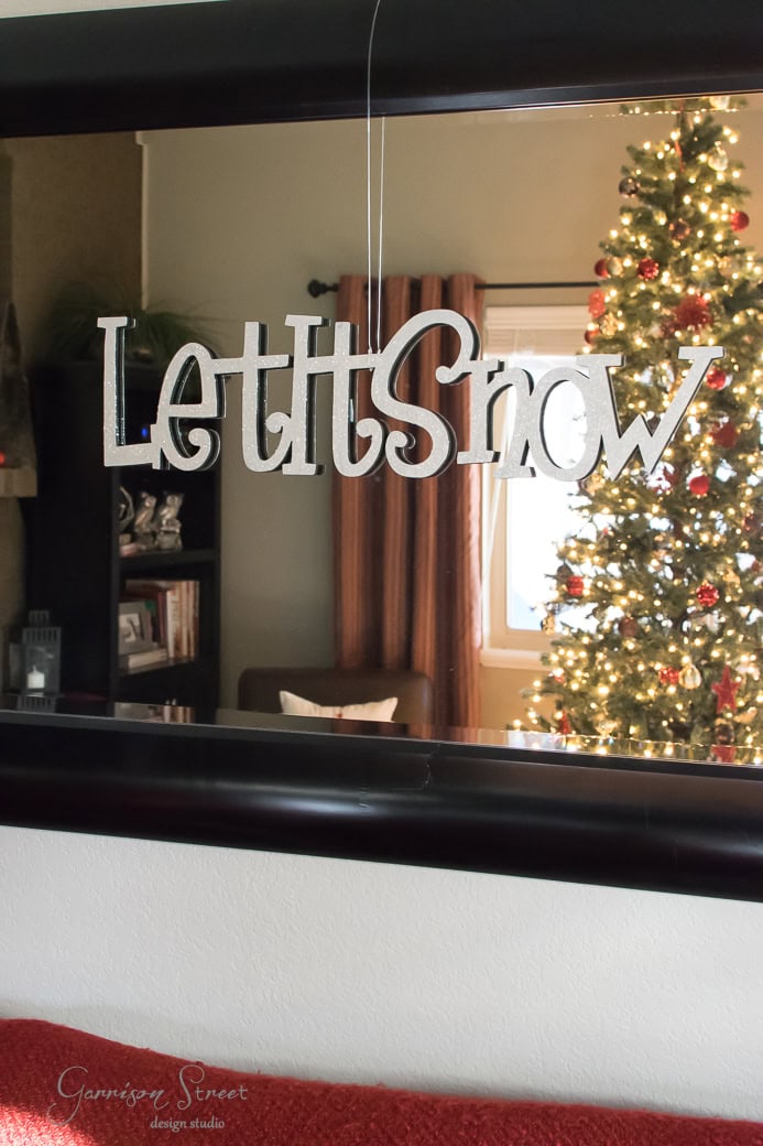 A festive sign with the words "Let it Snow" hangs on a wall. In the background, a decorated Christmas tree with lights is visible next to a window.