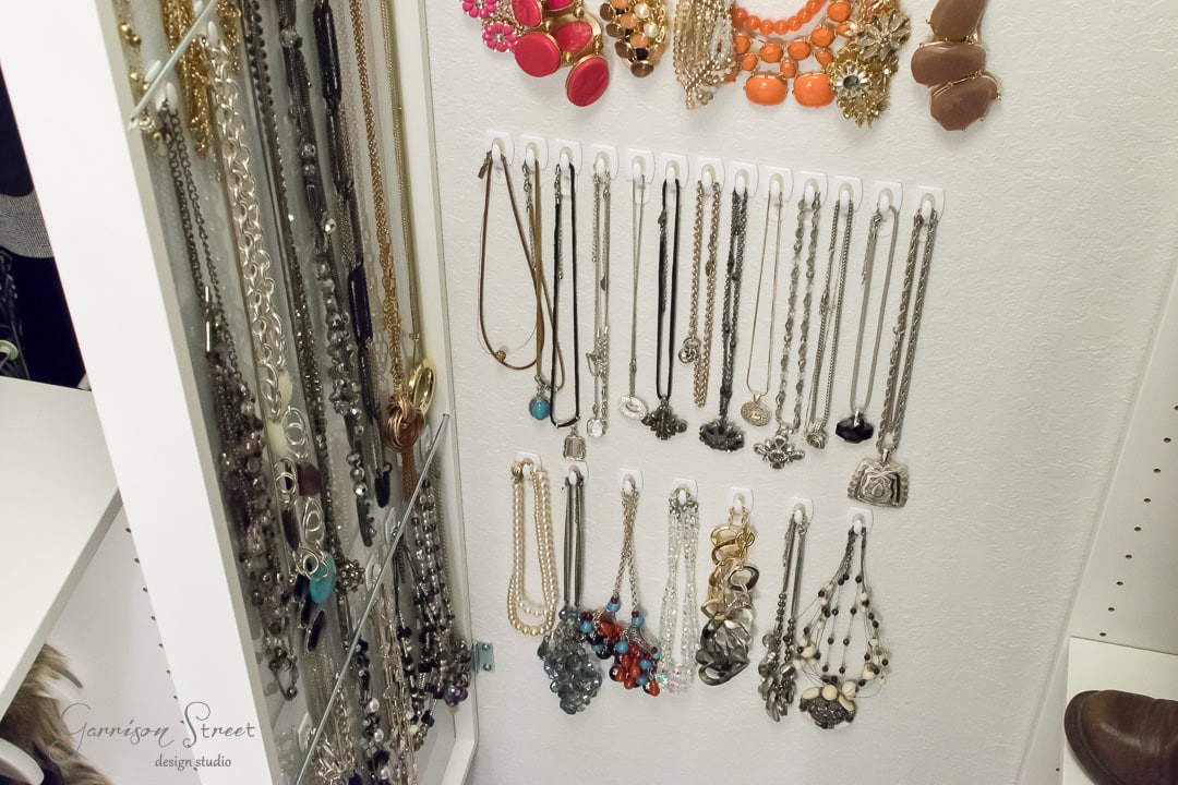 A variety of necklaces and bracelets are organized on a white Ikea wall-mounted jewelry hanger. The display includes metal chains, colorful beads, and pendants, arranged neatly in rows above a sleek mirror.