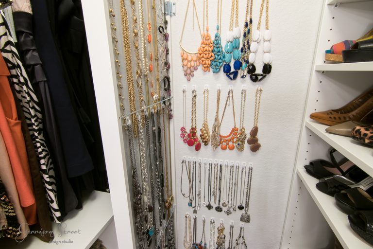 A neatly organized closet with various necklaces hanging on the wall. Shelves to the right hold shoes with different patterns, and to the left, colorful clothing is visible.