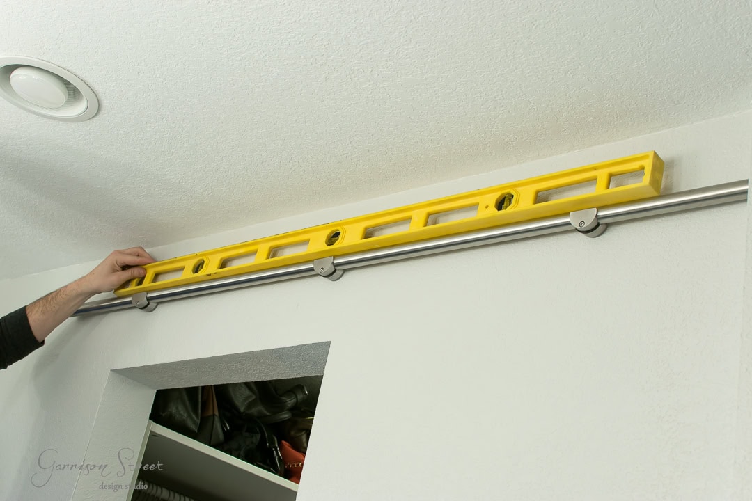 A person is using a yellow spirit level to perfectly align a metal rail for a barn door mounted above a doorway in a room with pristine white walls.