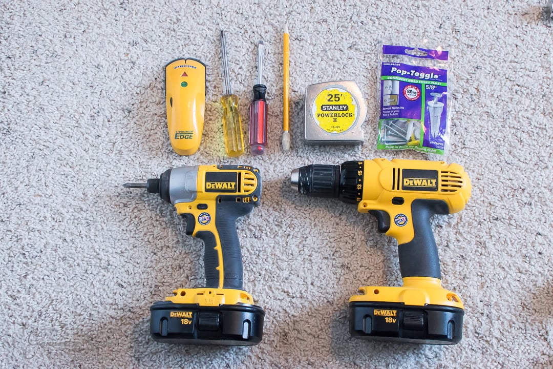 A set of tools displayed on a carpet: two yellow cordless drills, a stud finder, two screwdrivers, pencils, a measuring tape, wall anchors, and a level—perfect for installing your new barn door.
