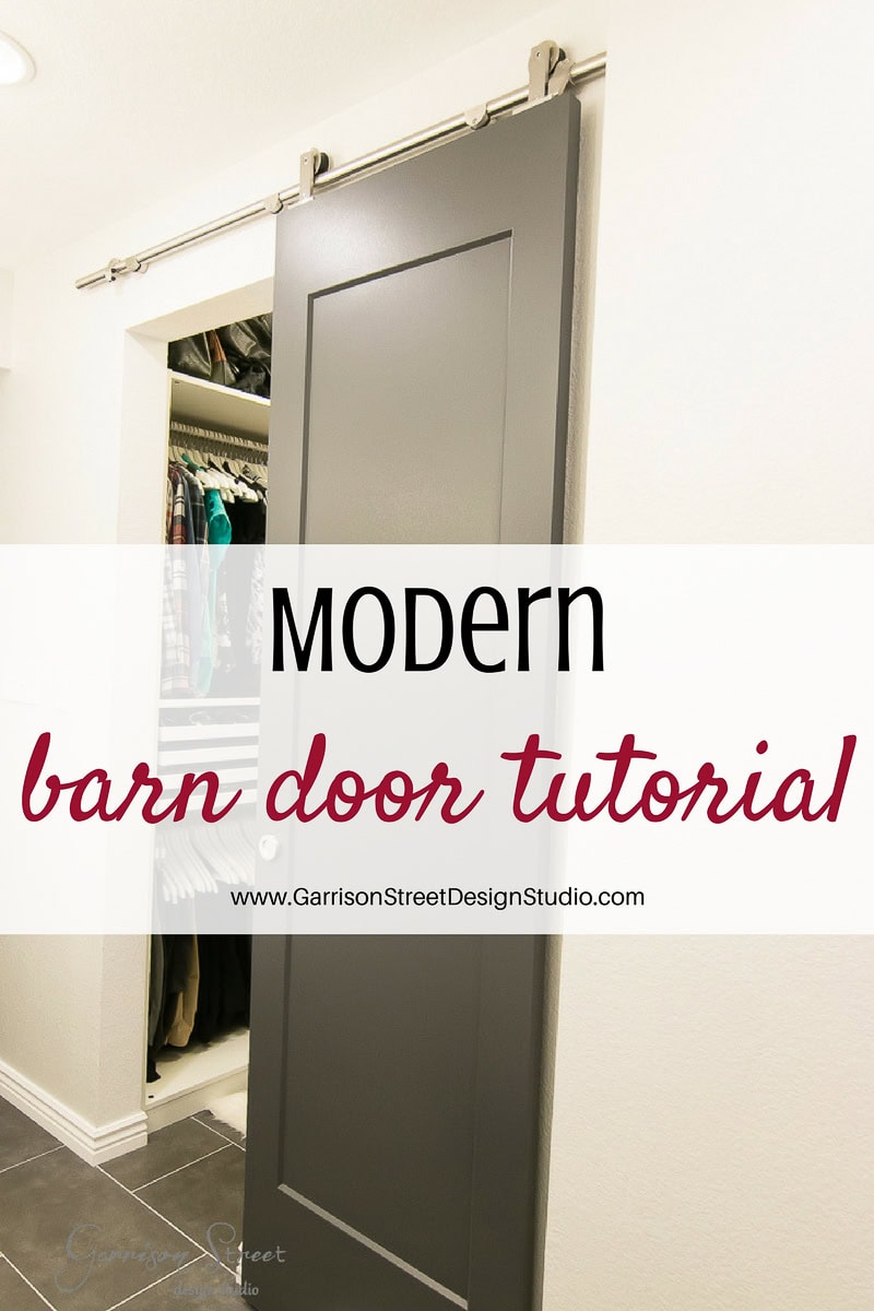 A sleek gray barn door on a sliding rail system stands partially open, unveiling a closet brimming with clothes. Text overlay reads, "Modern barn door tutorial" and "www.GarrisonStreetDesignStudio.com" at the bottom.