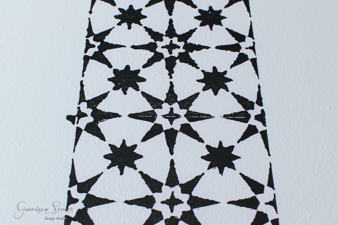A black star pattern is stenciled on a white canvas, featuring a series of repeated star shapes arranged in a geometric grid.