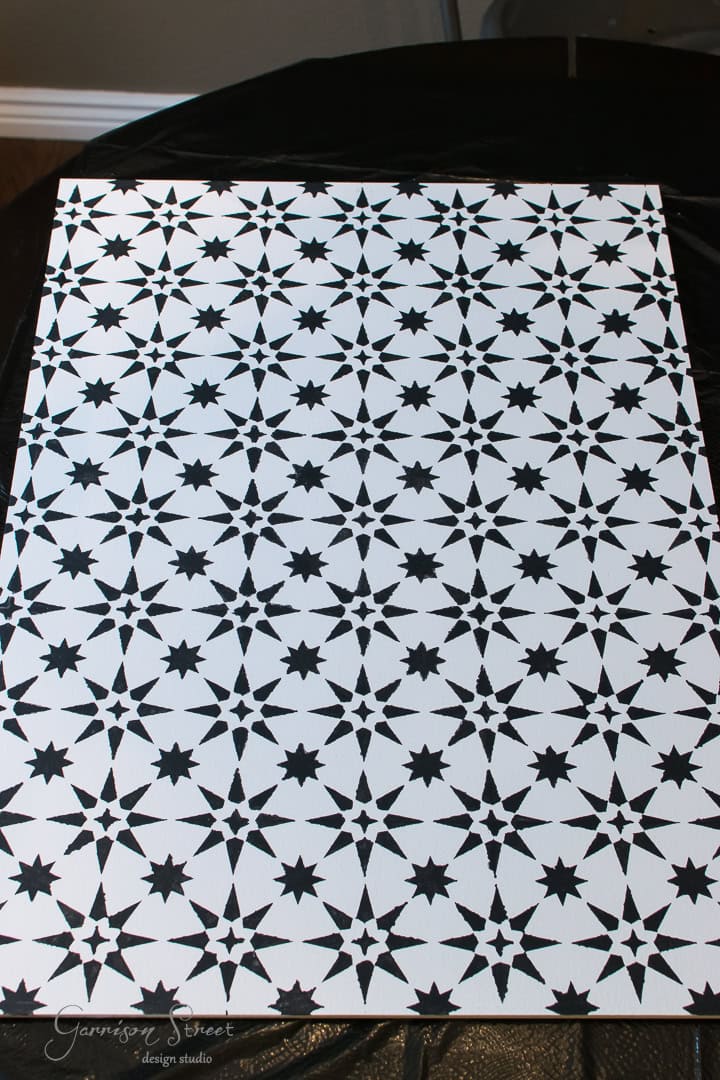 A white rectangular sheet with a repeating pattern of black geometric stars and diamonds, set against a dark surface.
