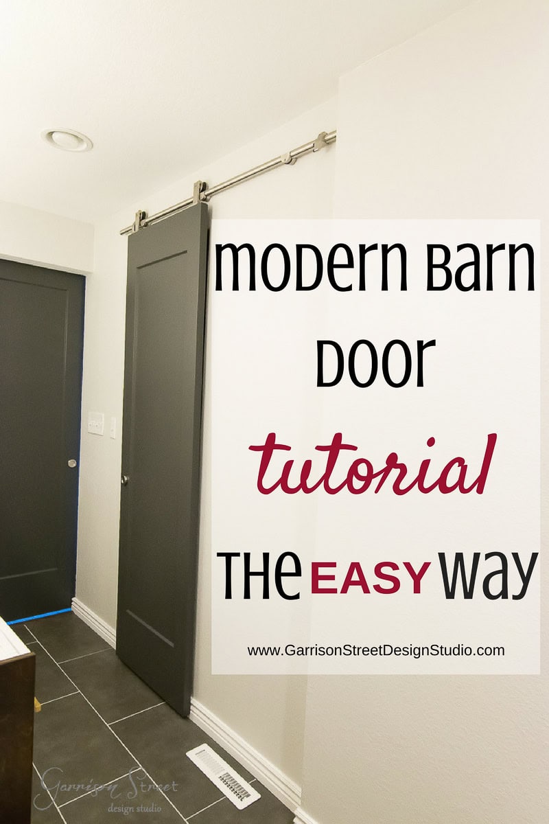 Modern interior with a dark barn door gliding smoothly on a metal rail. Wall text reads, "Modern Barn Door Tutorial The Easy Way" accompanied by a website link. The space showcases sleek white walls and elegant dark floor tiles.