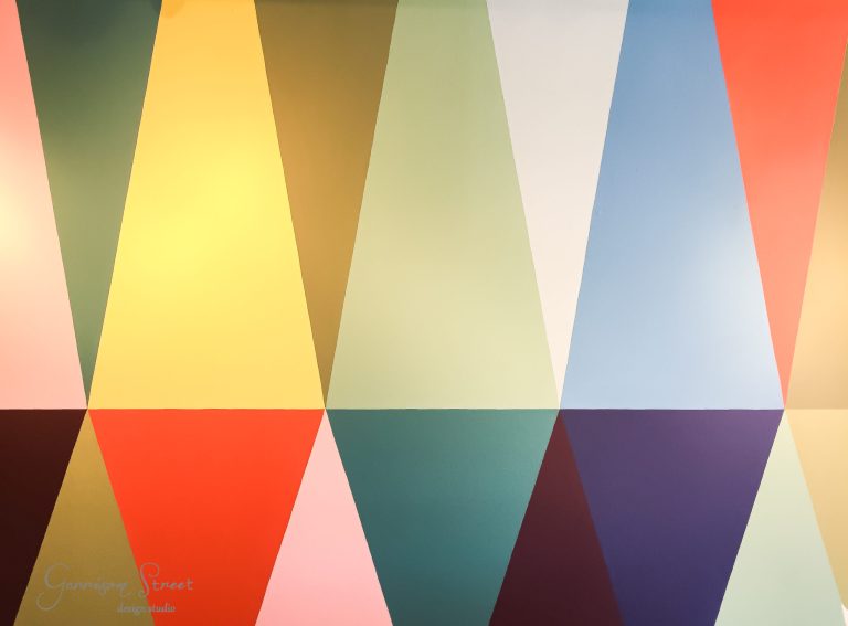 Colorful abstract geometric pattern featuring a grid of triangles and hexagons in various shades of yellow, green, blue, red, and orange. The design creates a vibrant and visually dynamic composition.