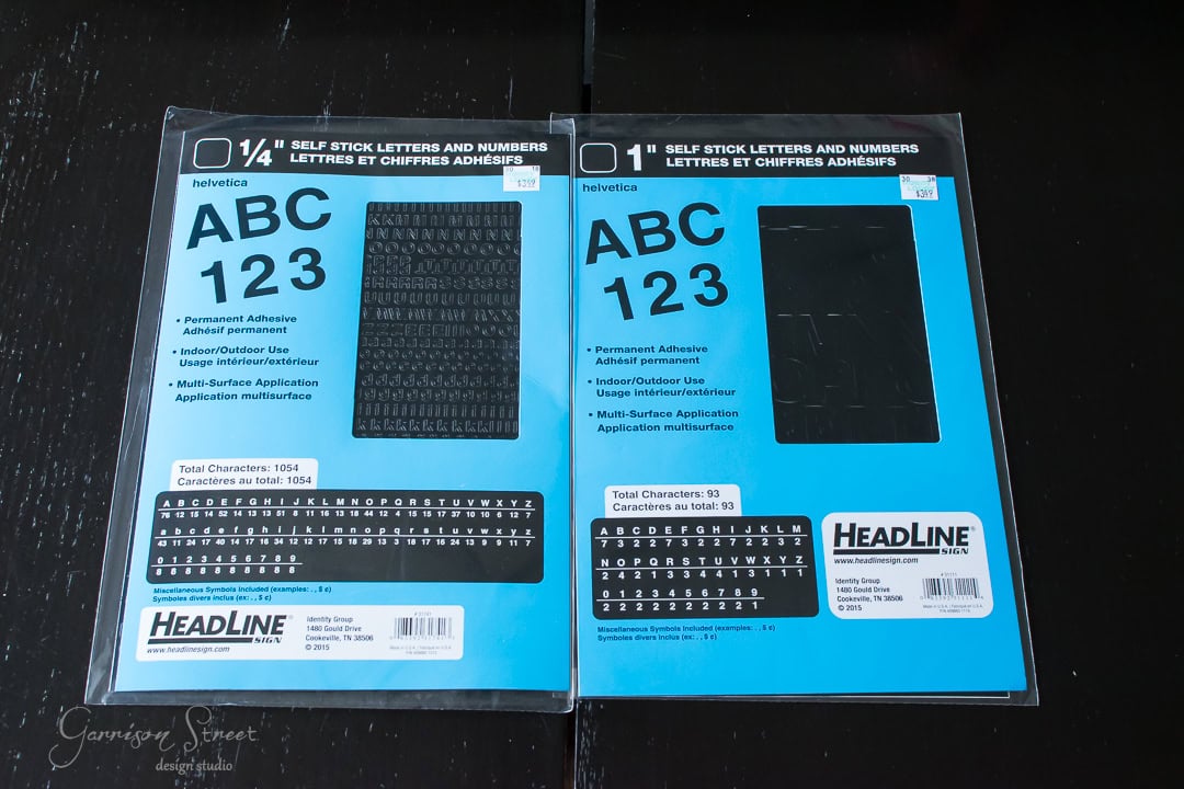 Two packages of Helvetica self-stick letters and numbers on a black surface. The left package features 1/4" characters, while the right package shows 1" characters. Both have blue labels with sample characters and product details.