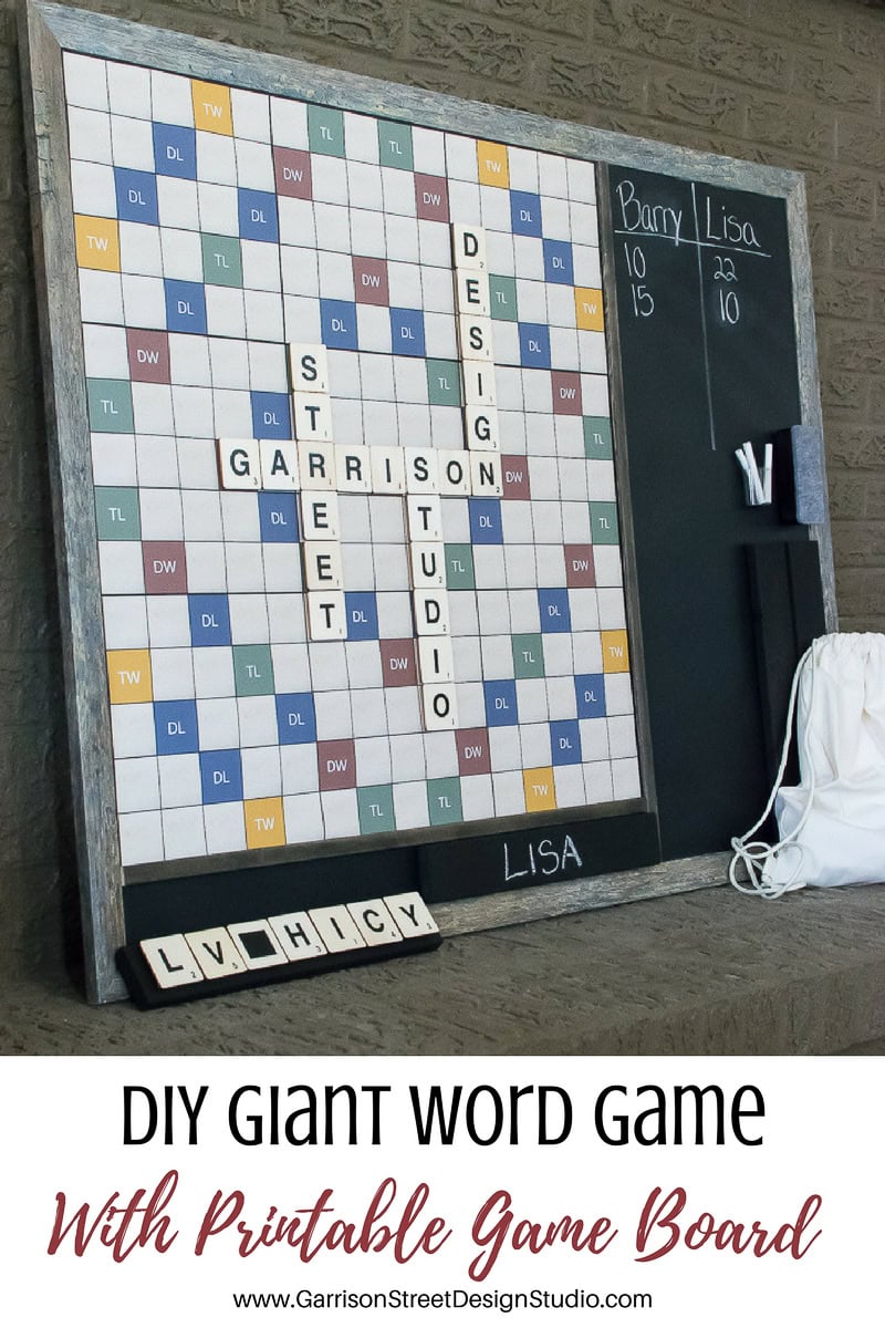 A giant DIY word game board on a stand with letter tiles spelling "Garrison Street Studio" and "Design." A chalkboard on the right shows scores for Barry and Lisa. A small white bag and additional letter tiles are nearby.