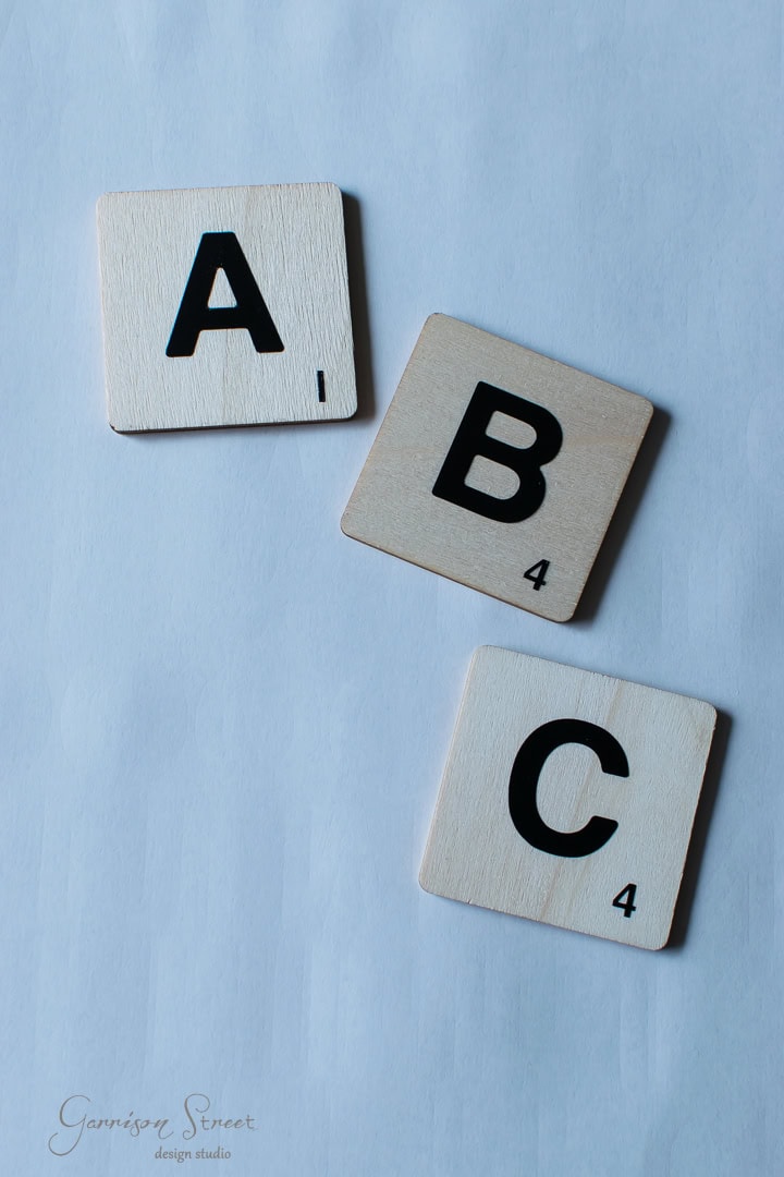 Three wooden Scrabble tiles on a light blue surface, displaying the letters A, B, and C with respective point values: A (1 point), B (4 points), C (4 points).