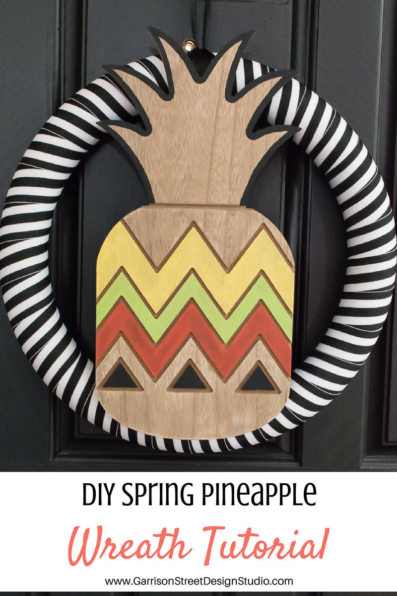 A decorative wreath featuring a wooden pineapple with yellow, orange, and green chevron patterns is wrapped in black and white striped fabric. Below, text reads: "DIY Spring Pineapple Wreath Tutorial" and a website link is visible.